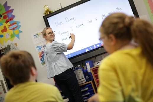 Young female teacher writing on a board and looking back at the class